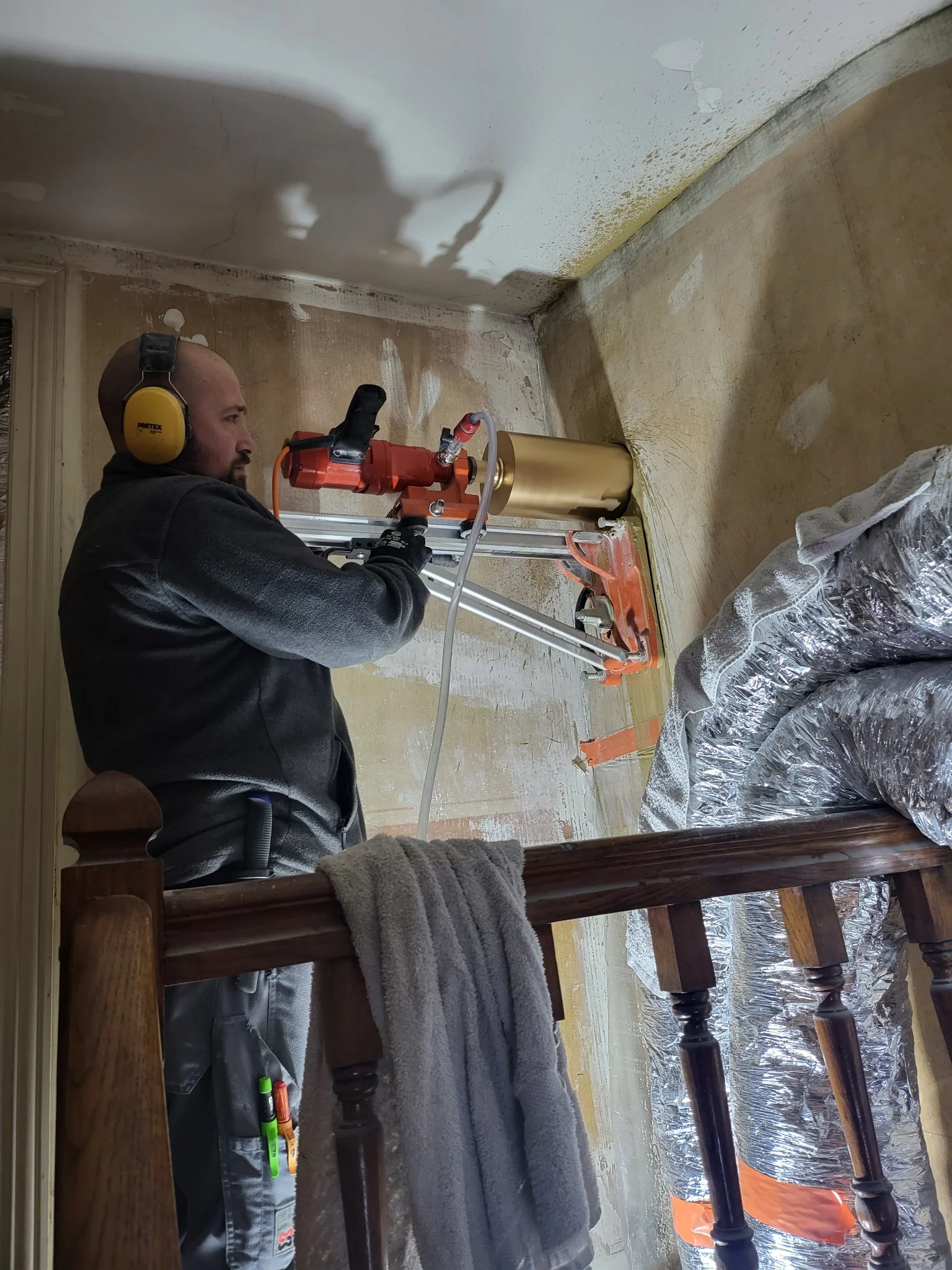 Thomas maury avec une grosse perceuse faisant un trou dans le mur